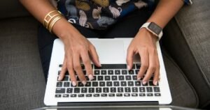 Hands typing on a laptop on a cozy sofa