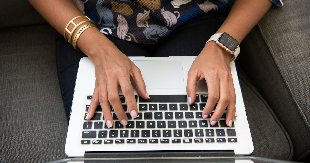Hands typing on a laptop on a cozy sofa