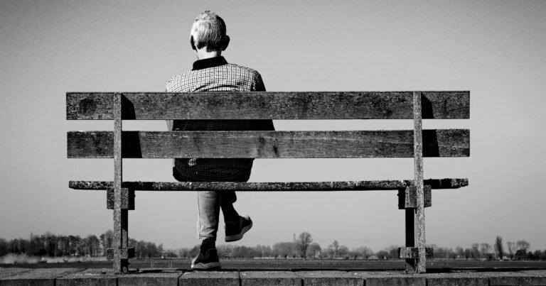 Person sitting alone on a bench, seen from behind