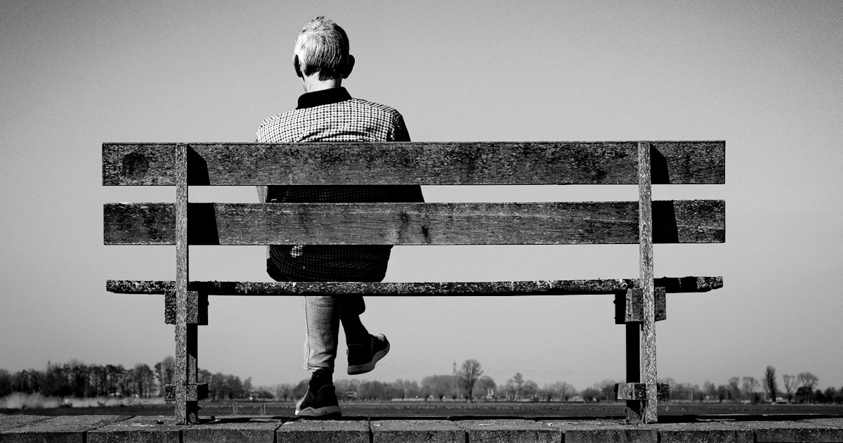 Person sitting alone on a bench, seen from behind