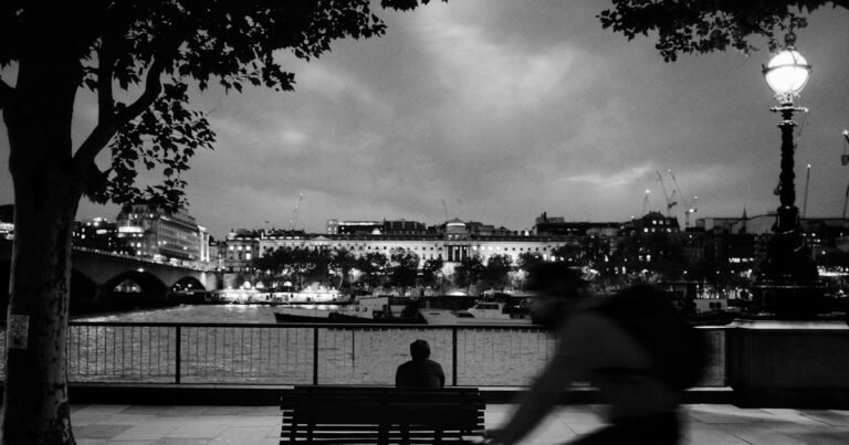 Person sitting alone on a riverside bench in black and white