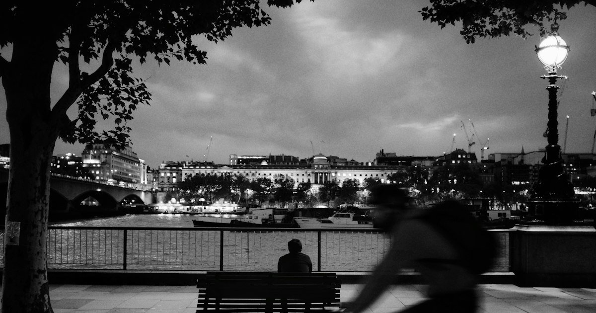 Person sitting alone on a riverside bench in black and white