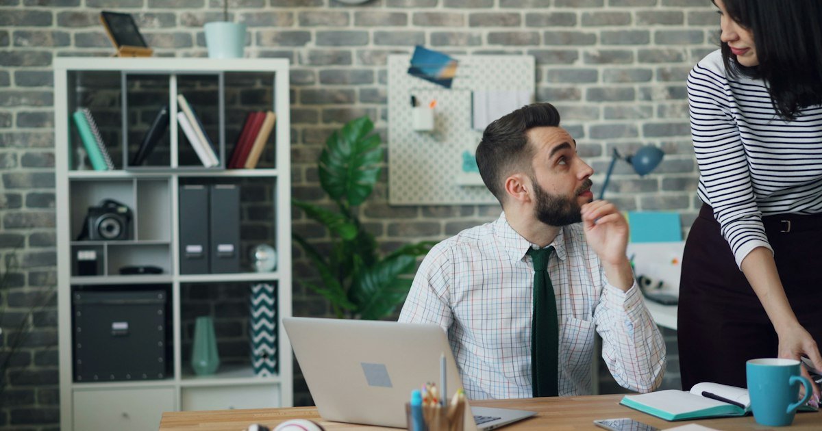 Man at his desk listening to feedback from a colleague