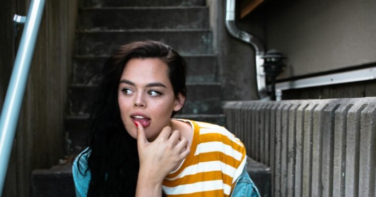 Young woman sitting on steps with a shy, thoughtful expression