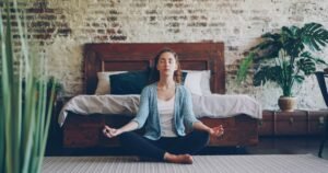 Woman meditating cross-legged on the floor of a calm bedroom