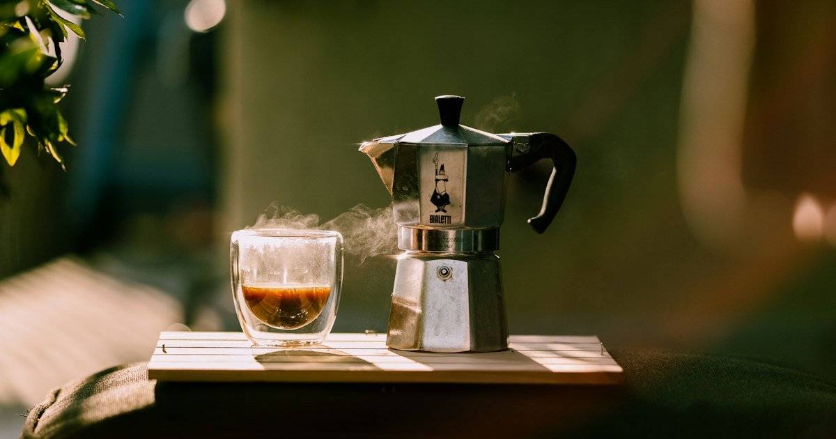 Cup of coffee and a moka pot in warm morning sunlight