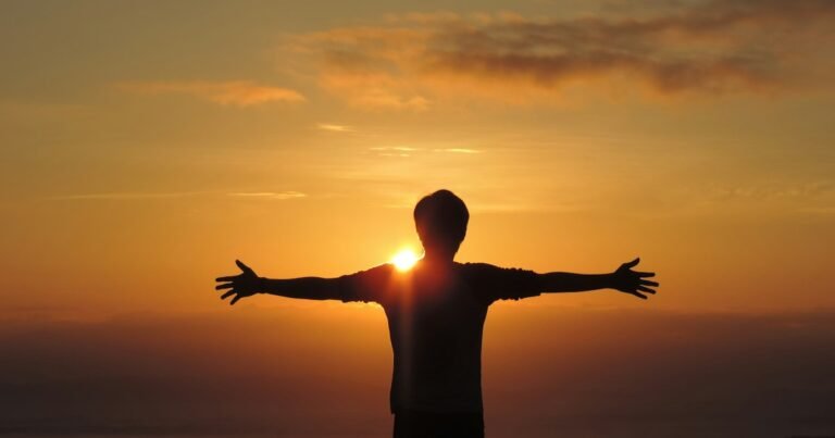 Person standing with arms outstretched against a golden sunset